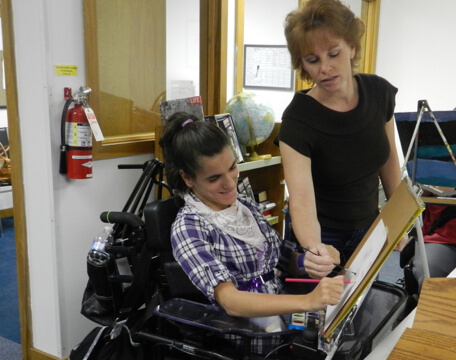 Woman helping young woman in wheelchair with painting